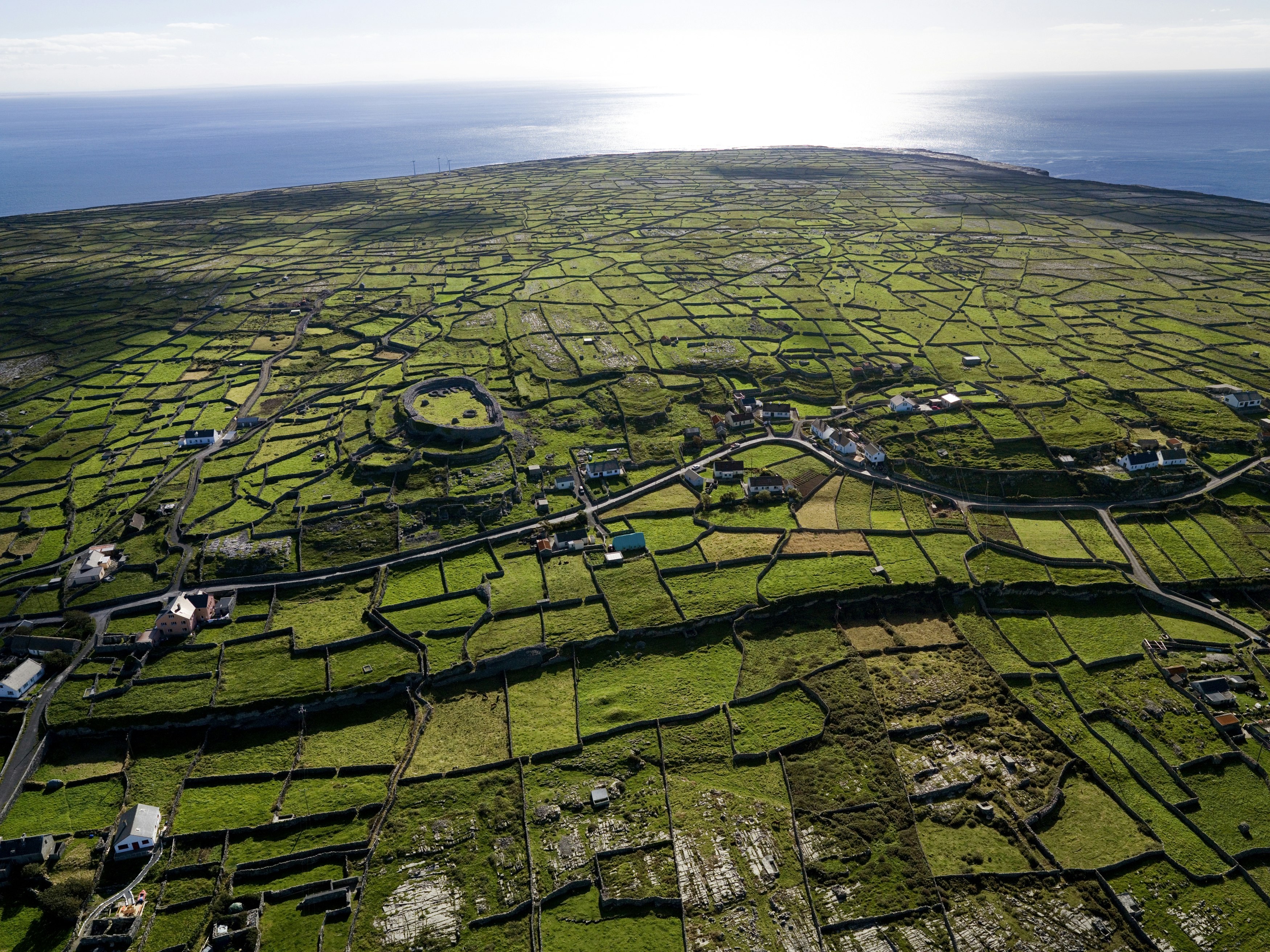 An aerial view of the island on a sunny day, including a prehistoric stone fort, green fields and stone walls 